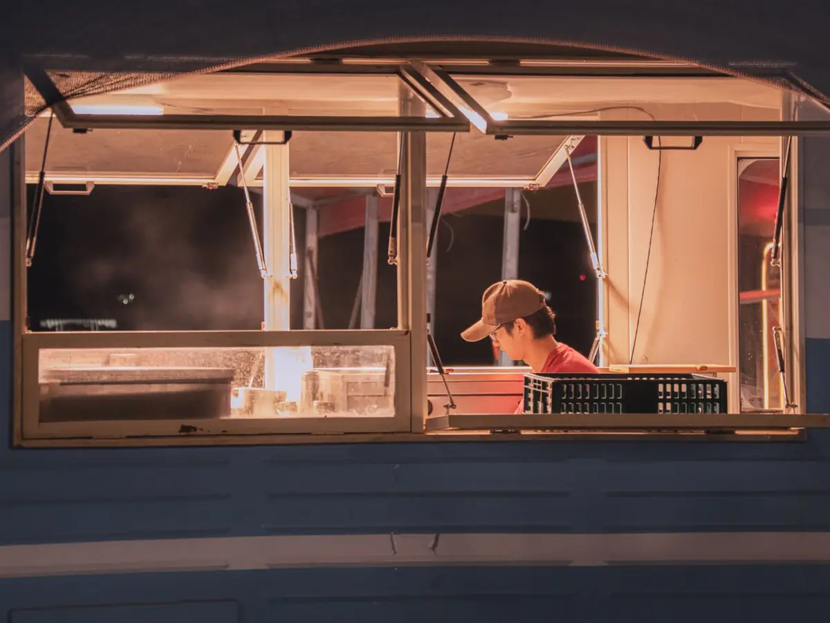 A cook working inside a food truck, seen through the service window